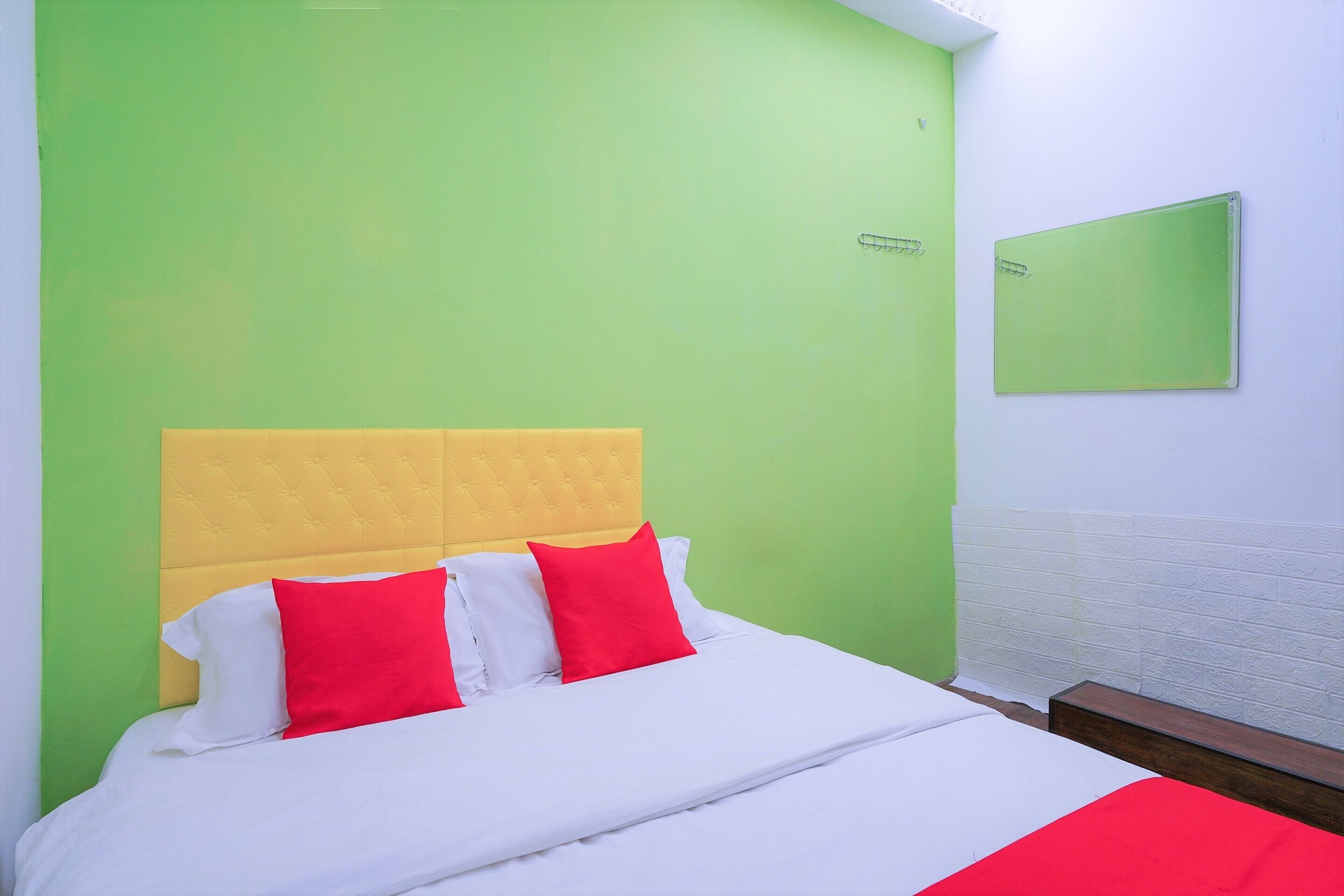 A bed with a yellow headboard, white and red pillows, and a green wall.
