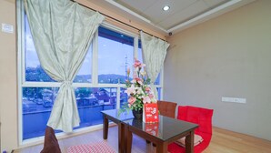 A room with a dining table, chairs, a red sofa, a window with curtains, and a vase with flowers. - Hotel O V Stay Guesthouse (George Town)