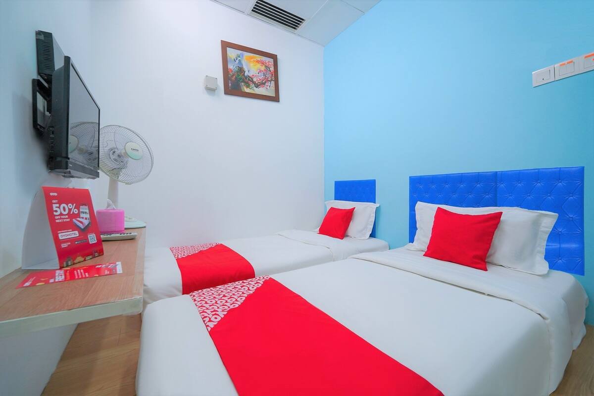 Une chambre d’hôtel avec deux lits, une télévision, un ventilateur fixé au mur et un tableau.