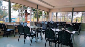 Un vaste espace de restauration intérieur, doté de nombreuses tables et chaises, et de grandes fenêtres offrant une vue sur les arbres et les bâtiments environnants.