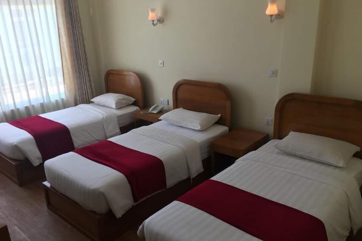 A hotel room with three single beds, each with a wooden headboard, white bedding, and a red accent. There are bedside lamps and a telephone on the nightstands.