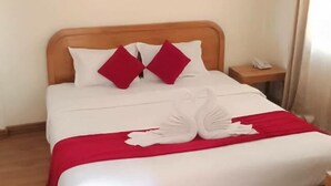 Un lit bien fait, avec une literie blanche et rouge, une tête de lit en bois et une petite table de chevet avec une lampe.