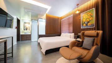 Een moderne hotelkamer met een groot bed, een massagestoel, een flatscreen televisie en een bloemschilderij aan de muur.