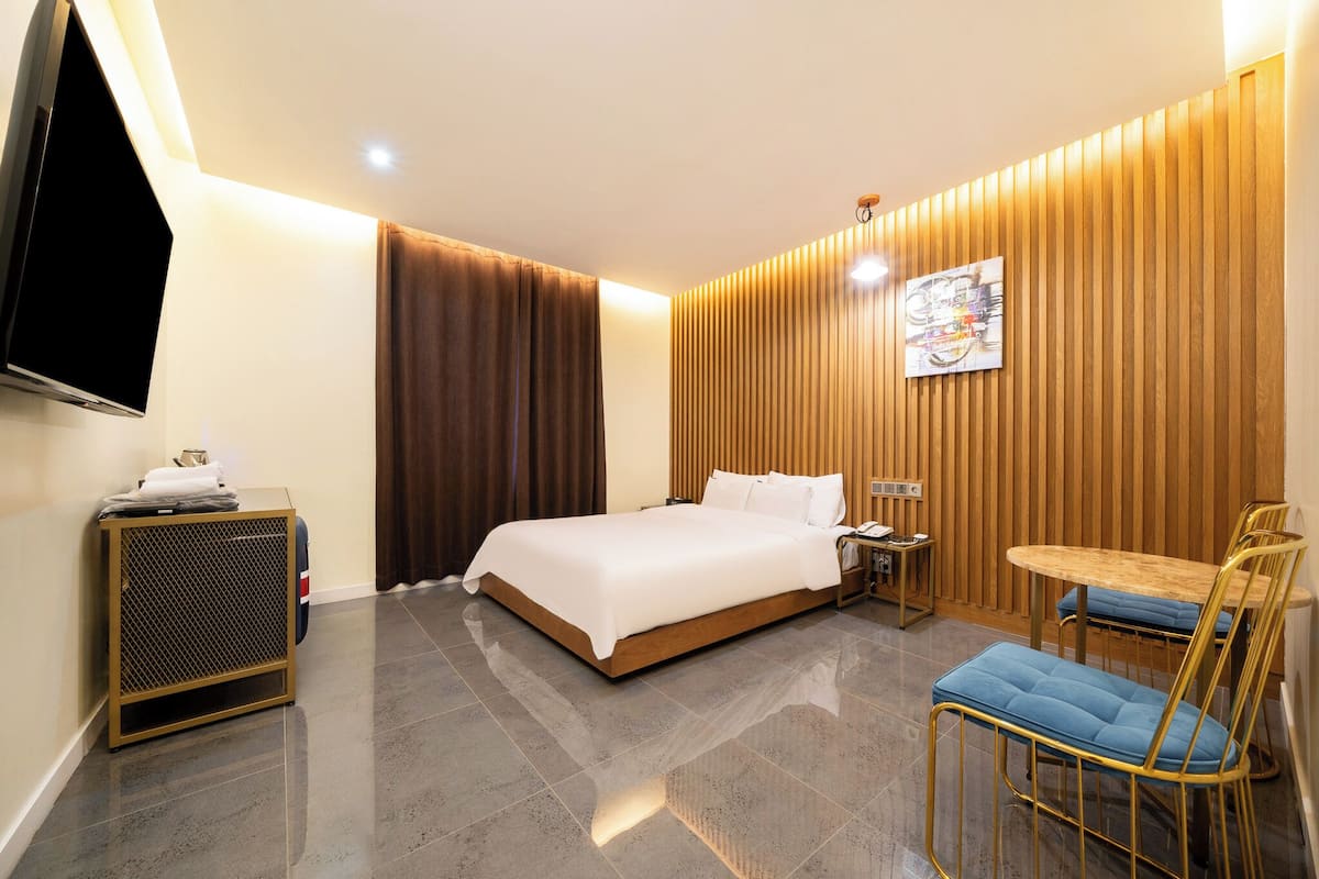 A hotel room with a bed, a desk, a chair, a TV, and a wall-mounted artwork.