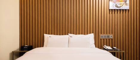 A hotel room with a wooden slat wall, a bed with white linens, a bedside table with a phone, and a painting above the bed.