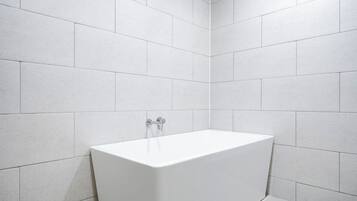 A modern bathroom with white tiles, a white bathtub, and a visible faucet.