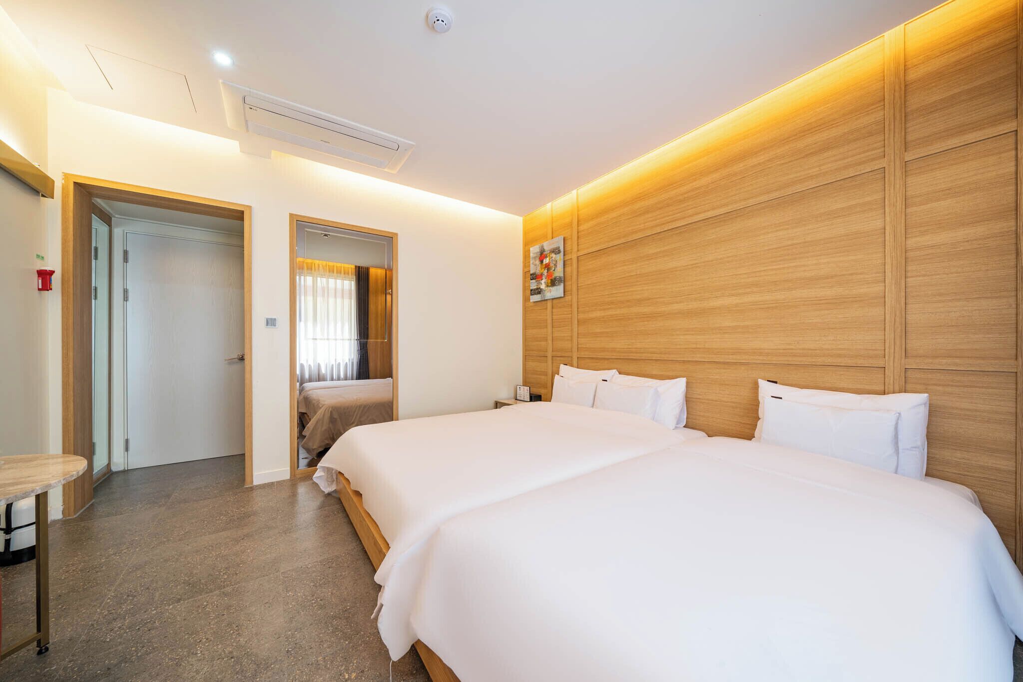 Una habitación de hotel moderna con una cama grande, un cabecero de madera y una mesita de noche pequeña.