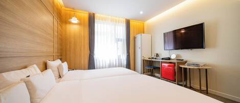 Habitación de hotel con una cama grande, un escritorio con computadora, televisor y un minibar rojo.