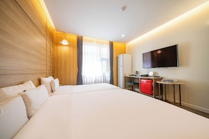Habitación de hotel con una cama grande, un escritorio con computadora, televisor y un minibar rojo.