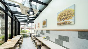 A modern restaurant with long communal tables and bar stools, a glass ceiling, and artwork on the walls.