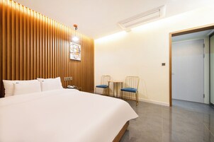 A hotel room with a large bed, wooden panel wall, two chairs, a small table, and a door.