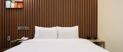 Quarto de hotel com parede de ripas de madeira, cama com roupa de cama branca, mesa de cabeceira com telefone e rádio, e um quadro sobre a cama.