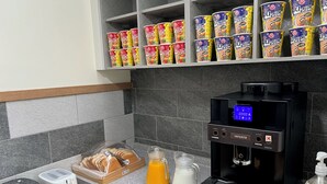 A kitchenette with a coffee machine, a bread display, and a shelf with canned drinks.