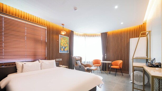 A modern hotel room with a large bed, two armchairs, a small table, and a desk with a chair.