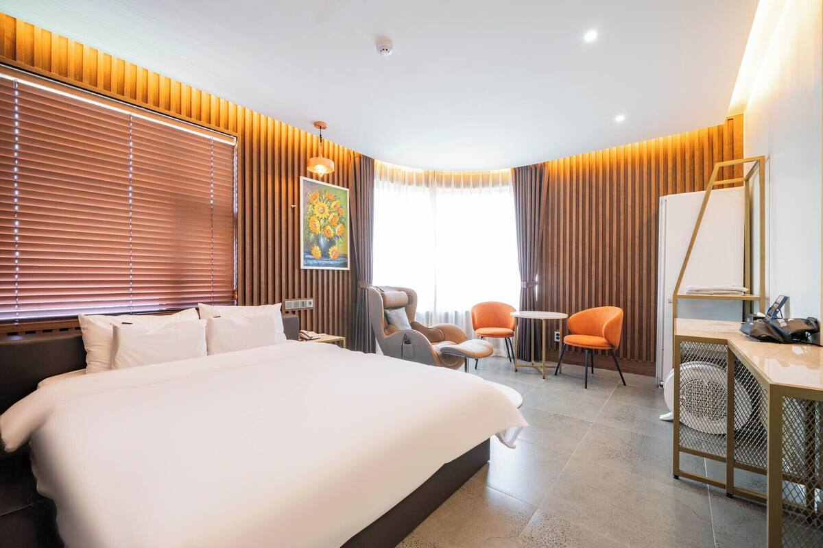 A modern hotel room with a large bed, two armchairs, a small table, and a desk with a chair.