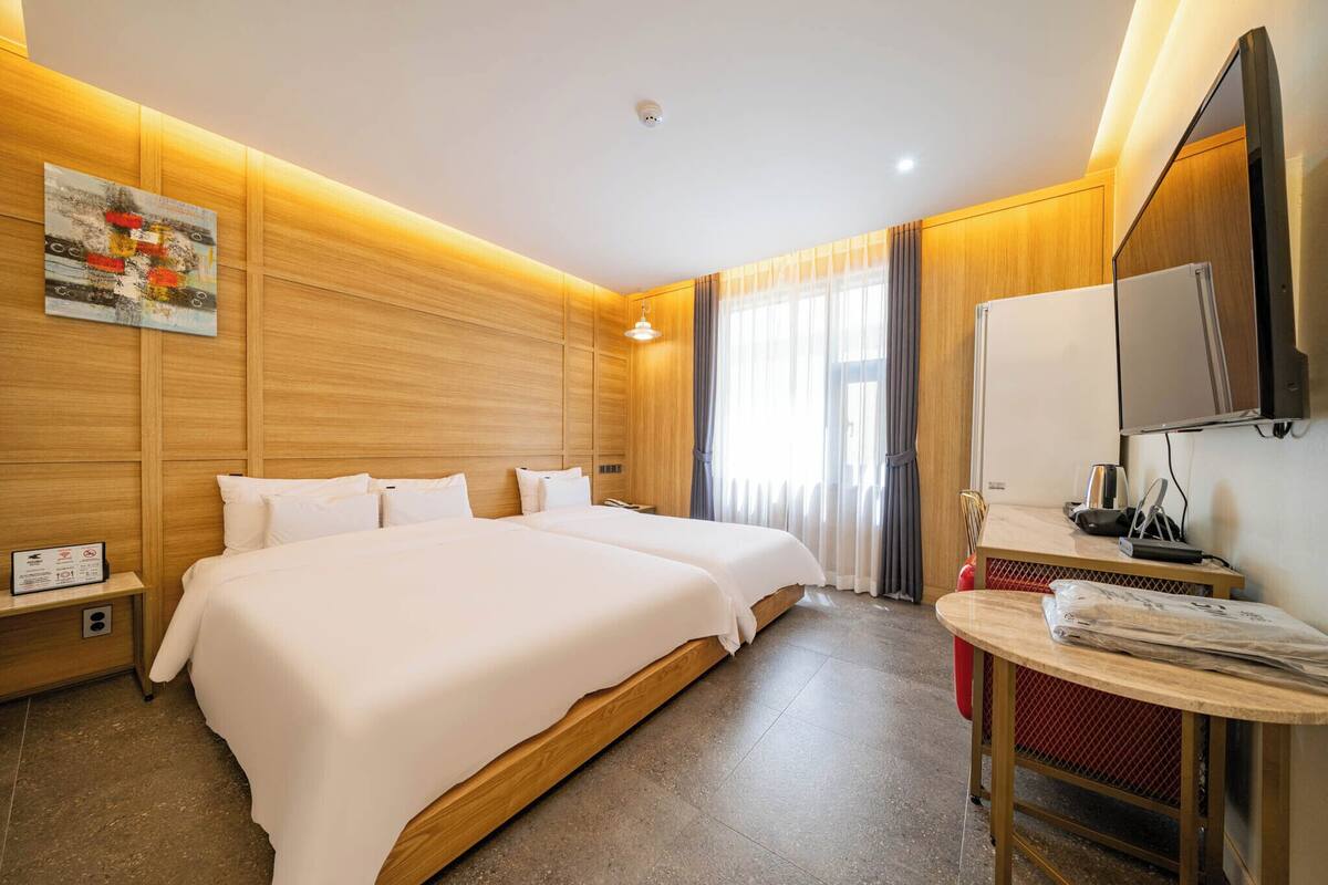 A hotel room with two beds, a TV, a small table, and a window with curtains.