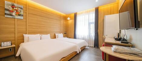 A hotel room with two beds, a TV, a small table, and a window with curtains.