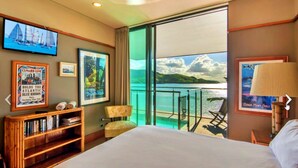 A hotel room with a large bed, a television, a bookshelf, a chair, and a balcony with a view of the sea. - Yacht Club 19 Bijou De Mer 2 Buggies (Whitsundays)