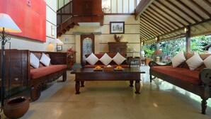 A spacious lobby with a central coffee table, two sofas with cushions, a wooden cabinet, and a staircase. - Rumah Ganesha (Ubud)