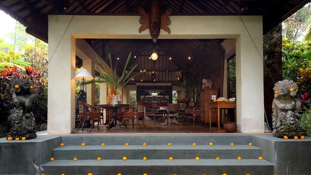 A covered outdoor seating area with a table and chairs, surrounded by steps adorned with marigold flowers. - Rumah Ganesha (Ubud)