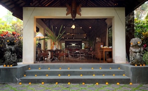 A covered outdoor seating area with a table and chairs, surrounded by steps adorned with marigold flowers. - Rumah Ganesha (Ubud)