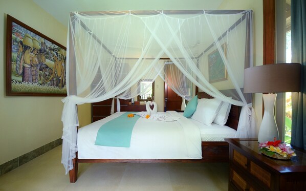 A bed with a canopy, a painting on the wall, and a nightstand with a lamp. - Rumah Ganesha (Ubud)