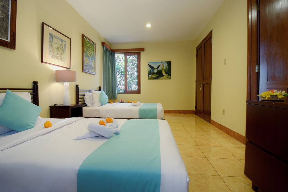 A hotel room with two beds, a nightstand, a lamp, and artwork on the walls.