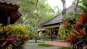 A garden pathway leading to a traditional-style building with a tiled roof, surrounded by lush tropical plants. - Rumah Ganesha (Ubud)