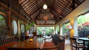 An indoor dining area with a high ceiling, wooden furniture, and a view of the garden. - Rumah Ganesha (Ubud)