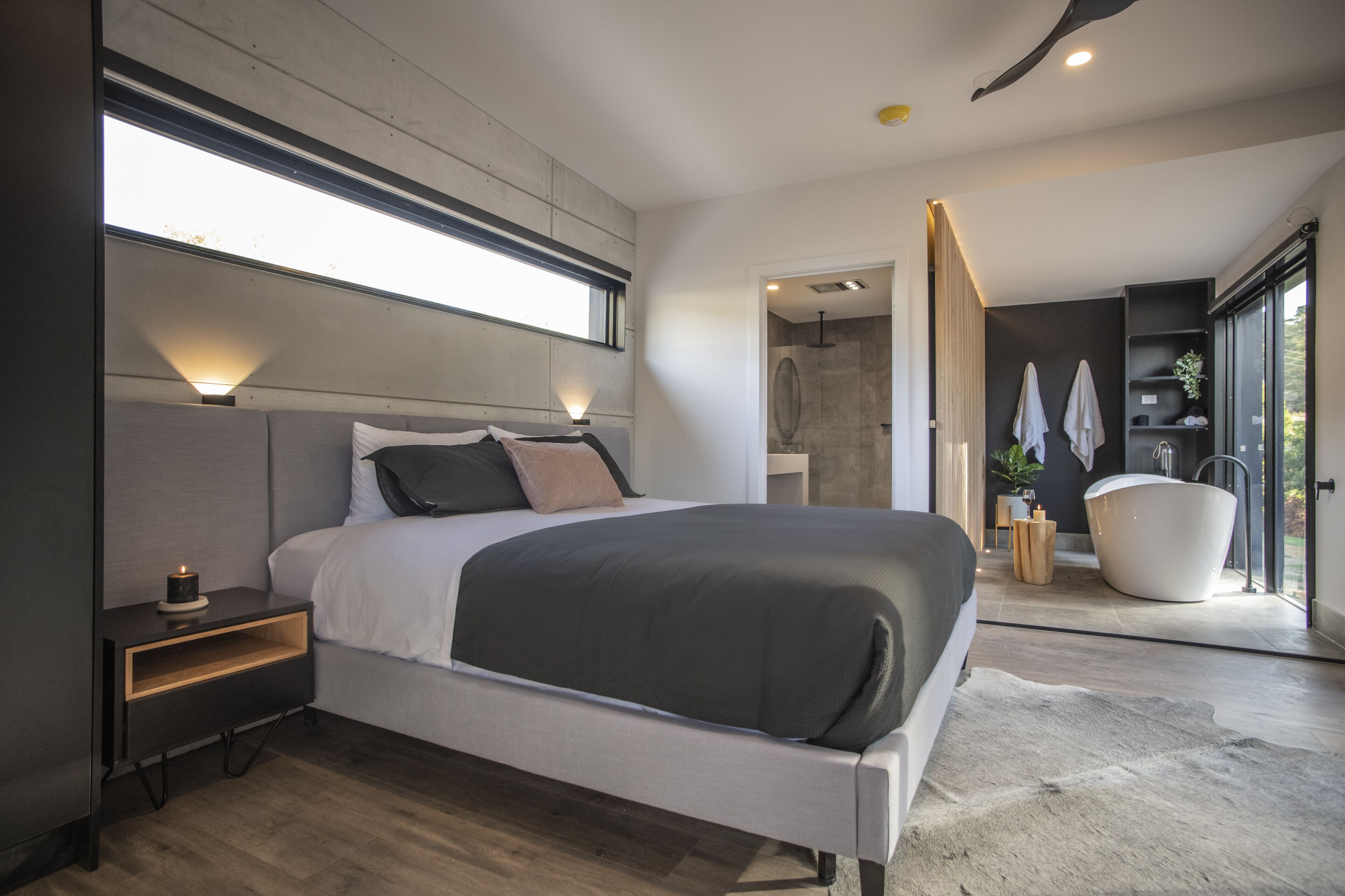 Un dormitorio moderno con una cama grande, lámparas de noche, una estantería empotrada y vistas al baño.