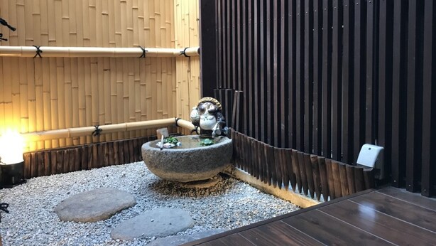 Ein traditioneller japanischer Garten mit einem Steingefäß, einer Bambuswand und einem hölzernen Deck.