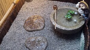 Ein traditionelles japanisches Onsen mit einem Steinhotspring, einer kleinen Holzplattform und einer dekorativen Eulenstatue.