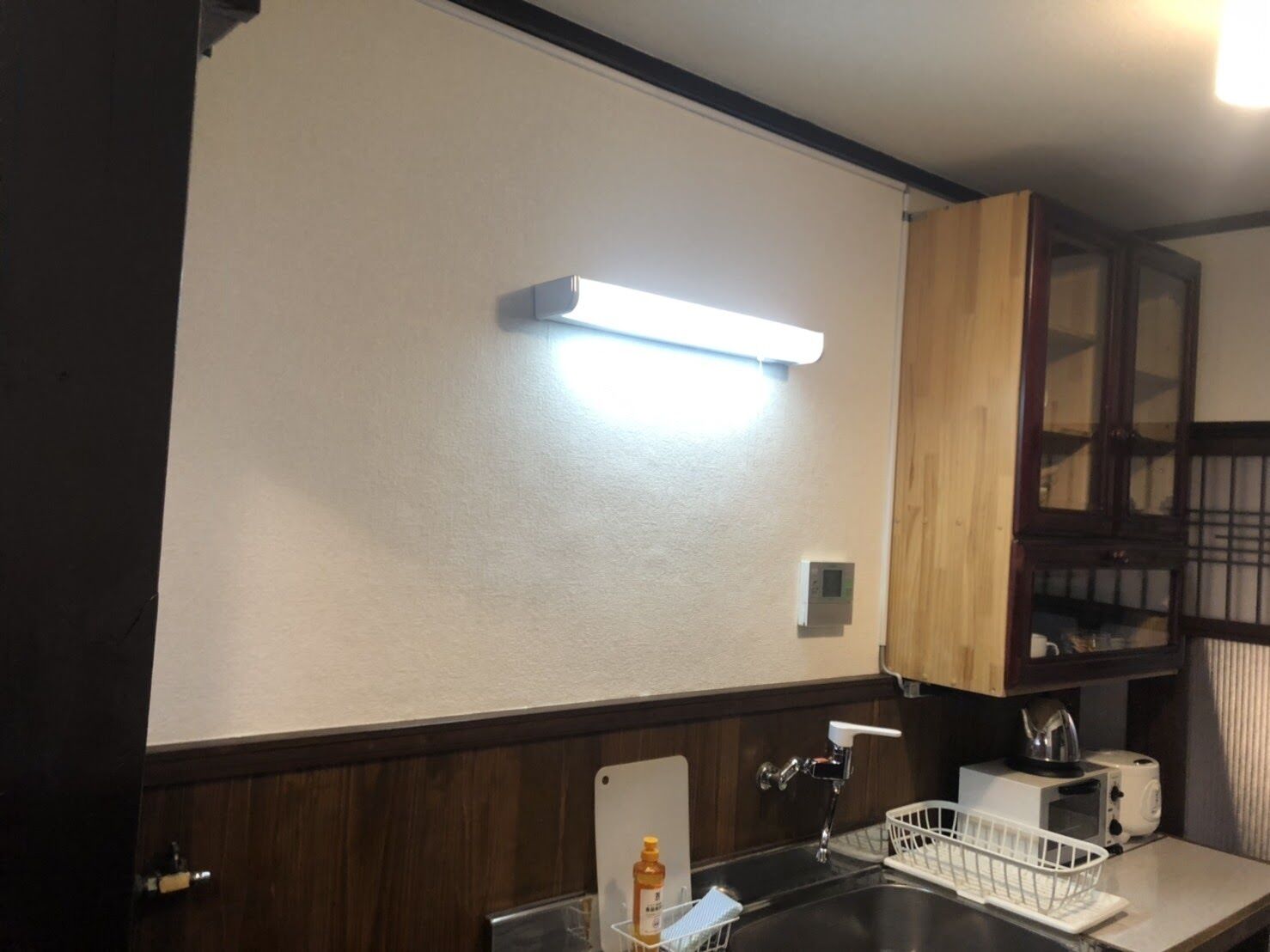 A kitchen with a white countertop, a sink, a microwave, a toaster, and wooden cabinets.