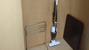 A small, enclosed closet with a vacuum cleaner, a metal drying rack, and a hanging clothes rack.