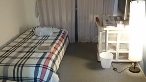 A hotel room with a bed, a desk with a lamp, a TV, and a window with curtains.