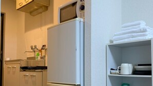 Una cucina compatta con frigorifero bianco, forno a microonde e ripiano con asciugamani e utensili da cucina.