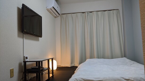 Una camera d'albergo con un letto, una scrivania con lampada, una TV a schermo piatto e un condizionatore d'aria.