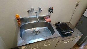A stainless steel sink with a drain, a bottle of dish soap, a sponge, and a black electronic device on the counter. - Uzumasa 206 (Kyoto)