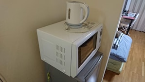 A microwave with a kettle on top, a small table with a chair, and a bed with a blue blanket. - Uzumasa 206 (Kyoto)