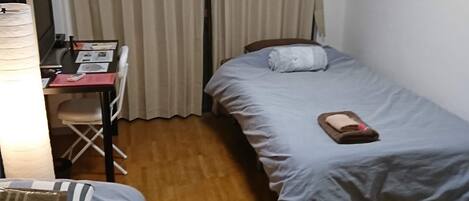 A small, compact room with two single beds, a desk with a chair, and a curtain-covered window.