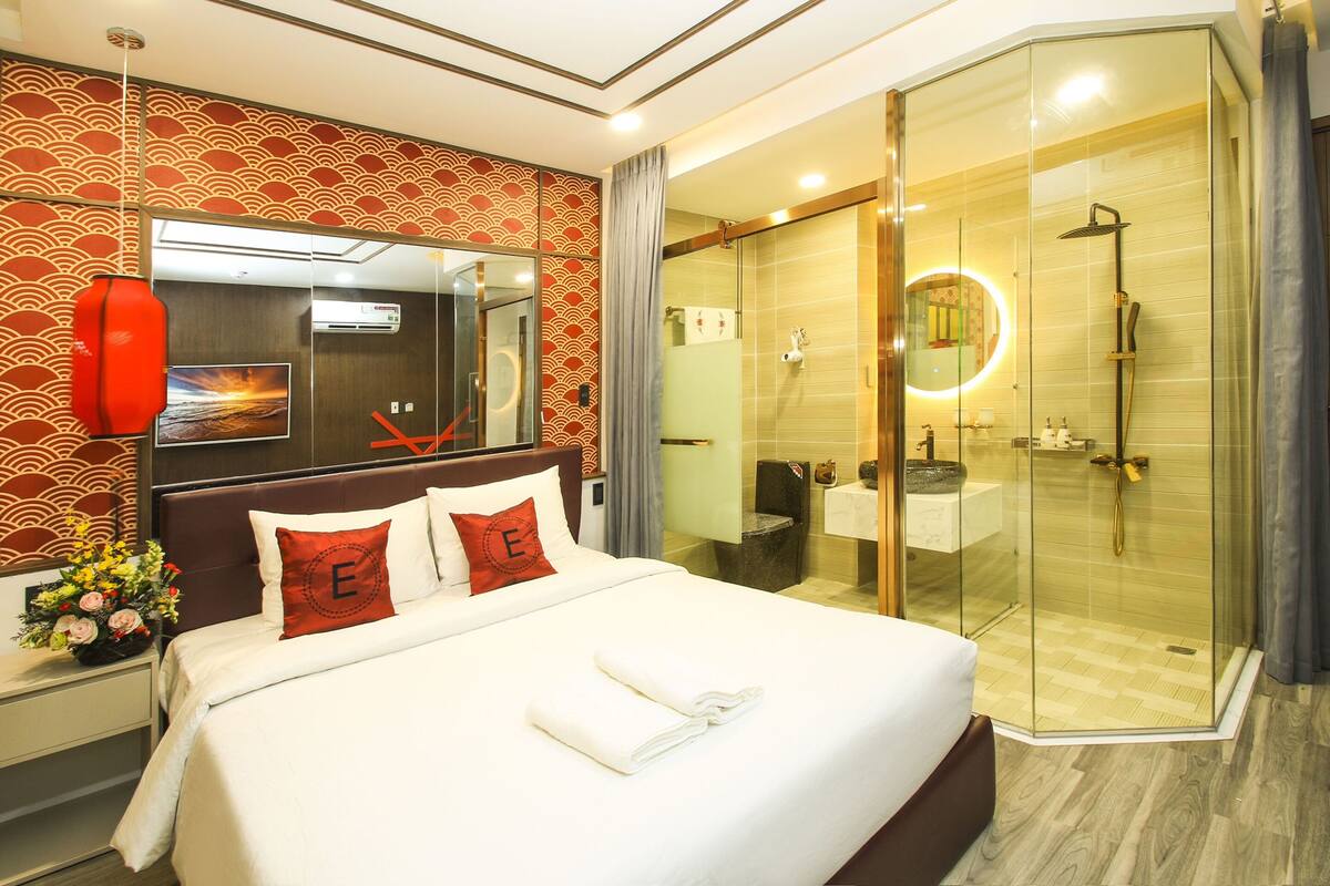 A hotel room with a large bed, a glass-enclosed shower, a mounted TV, and a decorative wall pattern.