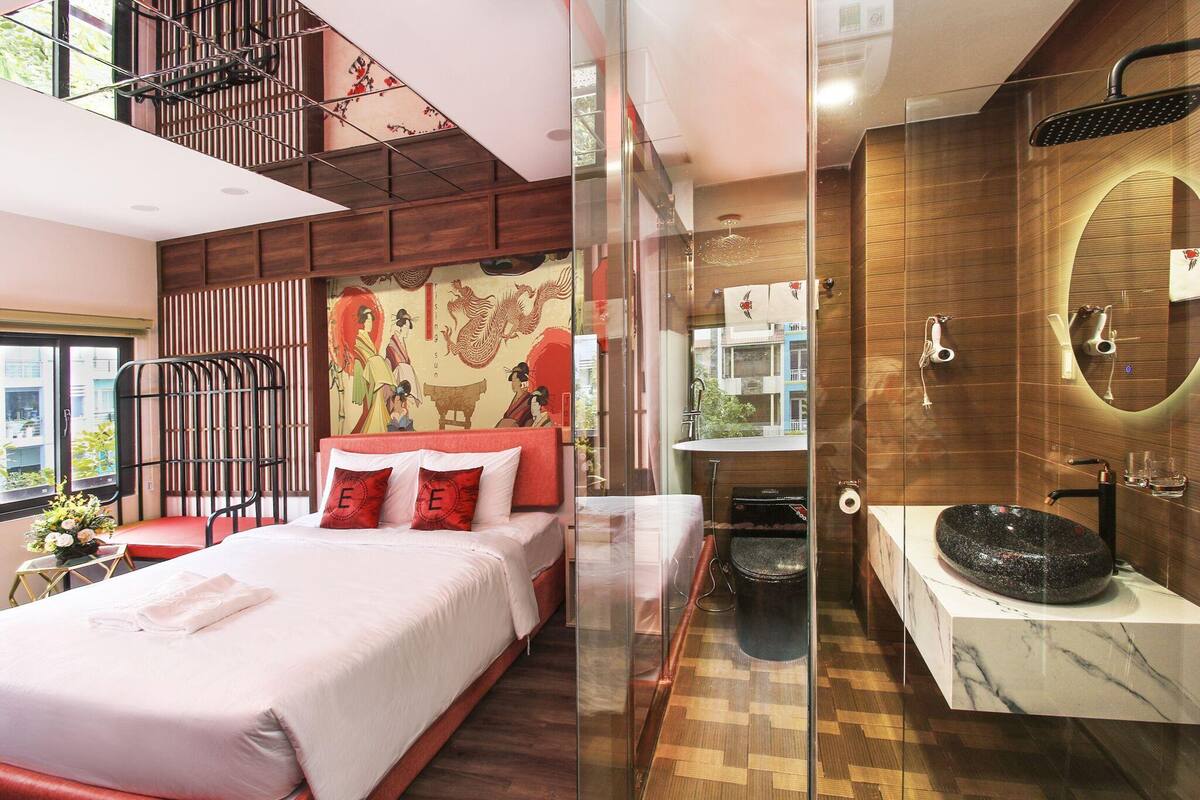 A modern hotel room with a large bed, a bathroom with a round sink, and a view of the city.