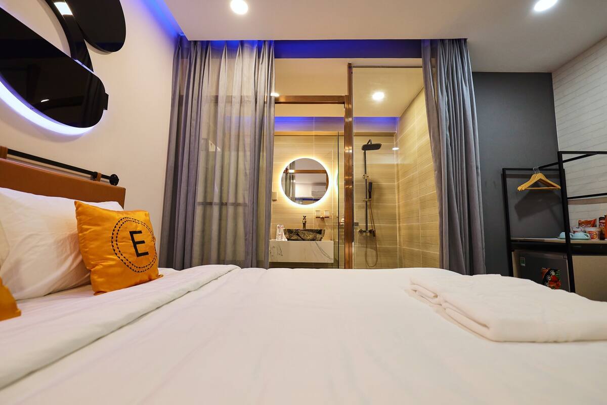 A hotel room with a bed, a bedside table, a mirror, a shower area, and a wardrobe.