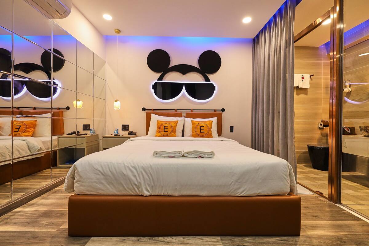 A modern hotel room with a large bed, a Mickey Mouse head decoration, and a mirror reflecting the room.