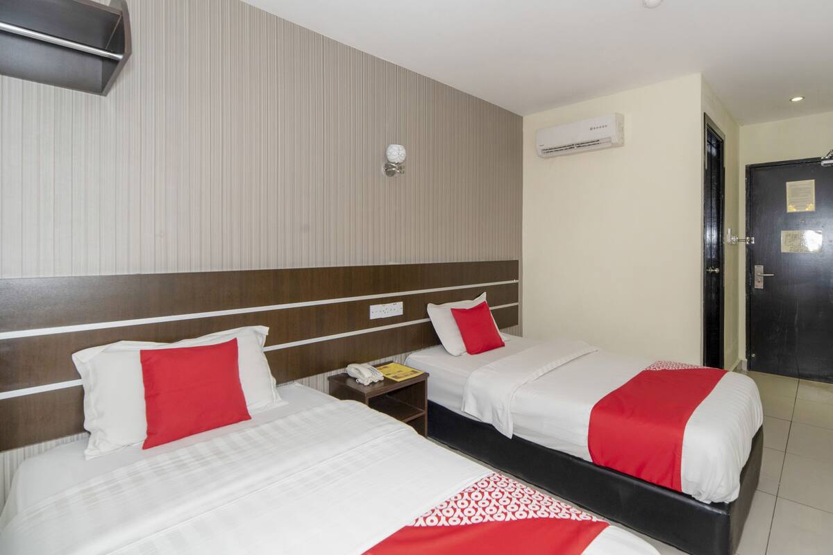 A hotel room with two beds, a bedside table with a phone and a notepad, an air conditioning unit, and a door with a notice.