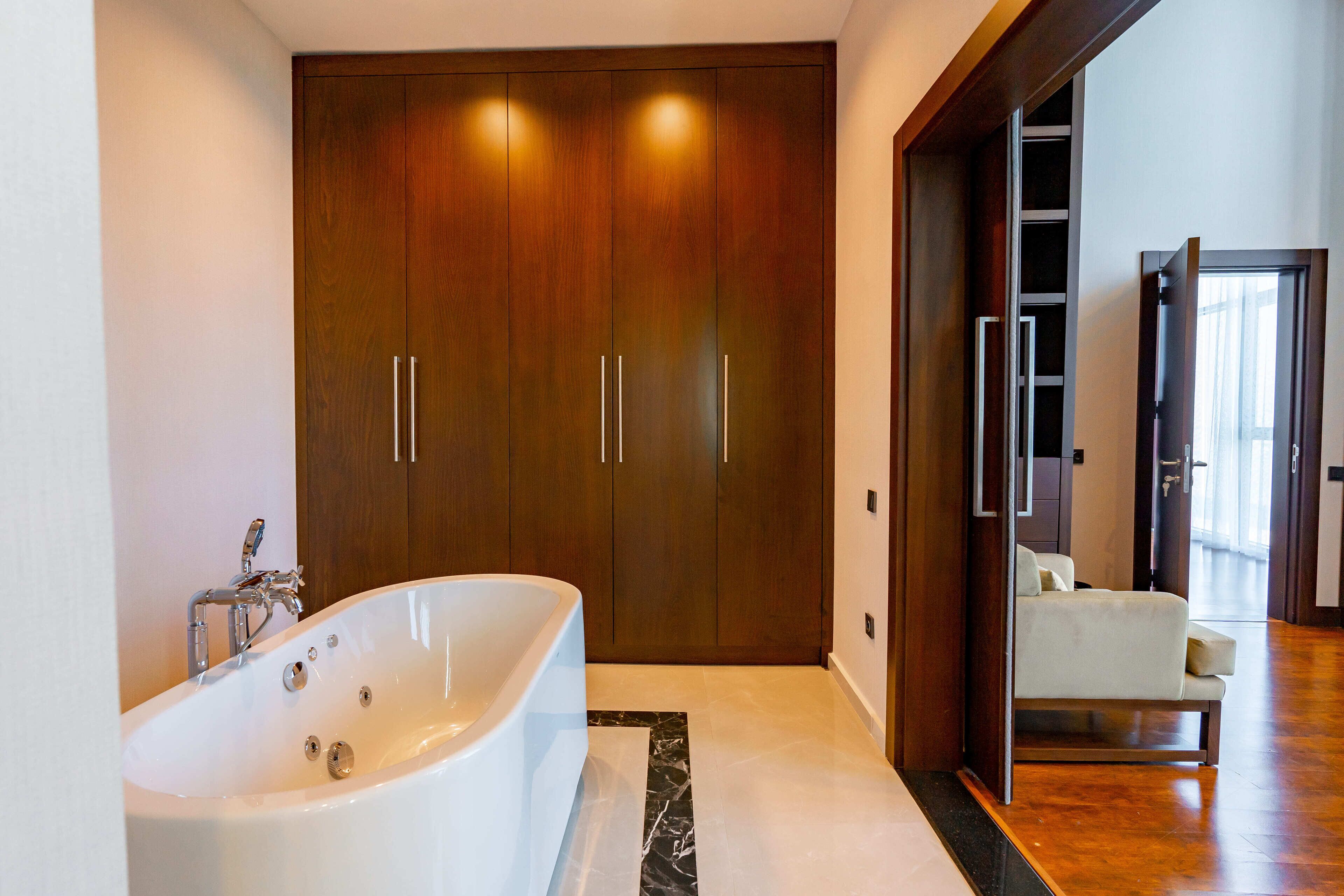 Une salle de bain moderne avec une baignoire sur pieds, un placard en bois et un coin salon avec un fauteuil.