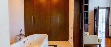 A modern bathroom with a freestanding bathtub, wooden wardrobe, and a seating area with a chair.