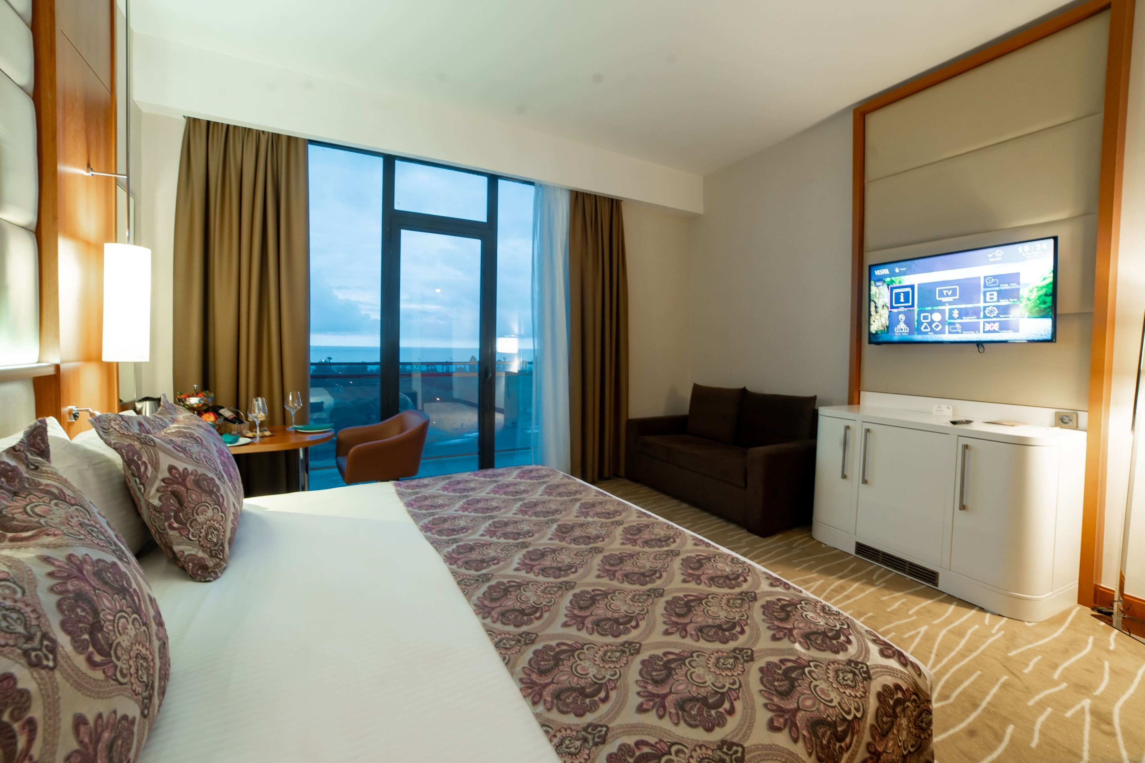 Habitación de hotel con una cama grande, televisión, escritorio con silla y vistas a la ciudad desde la ventana.