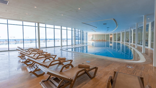 A large indoor swimming pool with sun loungers and a view of the ocean. -  Grand Bellagio Batumi Convention & Casino Hotel (Batumi)