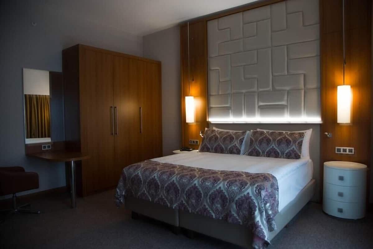 A hotel room with a large bed, a wooden wardrobe, a desk, and a nightstand.